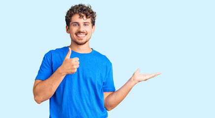 Young handsome man with curly hair wearing casual clothes showing palm hand and doing ok gesture with thumbs up, smiling happy and cheerful