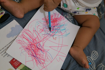 A toddler's hand is scribbling a drawing paper with his colorful markers