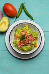 Mexican guacamole with chili pepper and tomato on turquoise background