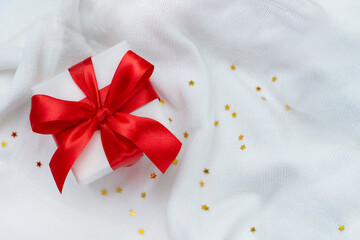 Christmas card with a red ribbon gift box and golden stars on a white background knitted sweater. Copyspace. Flat lay. Top view.