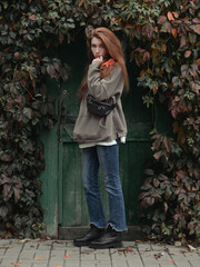 Full length portrait young redhead woman with autumn leaf in hand and fall red and yellow ivy background enjoying fall day
