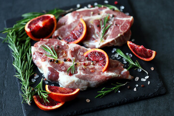 Selective focus. Macro. Raw pork steaks with rosemary and orange marinated on a stone board. Cooking meat steaks.
