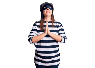 Young beautiful brunette woman wearing burglar mask begging and praying with hands together with hope expression on face very emotional and worried. begging.
