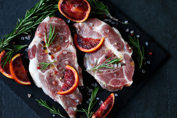 Selective focus. Macro. Raw pork steaks with rosemary and orange marinated on a stone board. Cooking meat steaks.