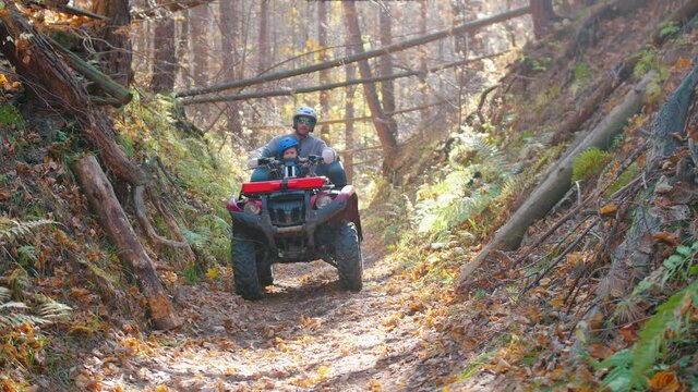 Outdoor activity - man climbs on the ATV with his son riding ATVs in the forest