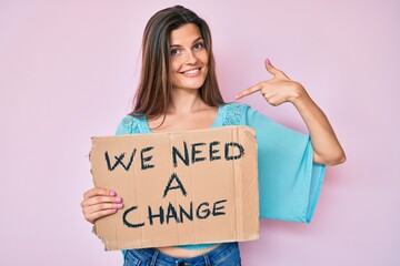 Beautiful caucasian woman holding we need a change banner pointing finger to one self smiling happy and proud