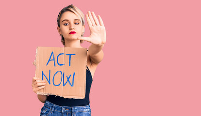 Young beautiful blonde woman holding act now banner with open hand doing stop sign with serious and confident expression, defense gesture