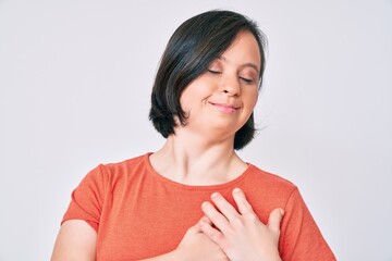 Brunette woman with down syndrome wearing casual clothes smiling with hands on chest with closed eyes and grateful gesture on face. health concept.