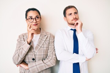 Beautiful couple wearing business clothes with hand on chin thinking about question, pensive expression. smiling and thoughtful face. doubt concept.