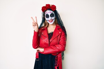 Woman wearing day of the dead costume over white smiling with happy face winking at the camera doing victory sign with fingers. number two.