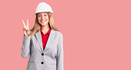 Beautiful young woman wearing architect hardhat showing and pointing up with fingers number two while smiling confident and happy.