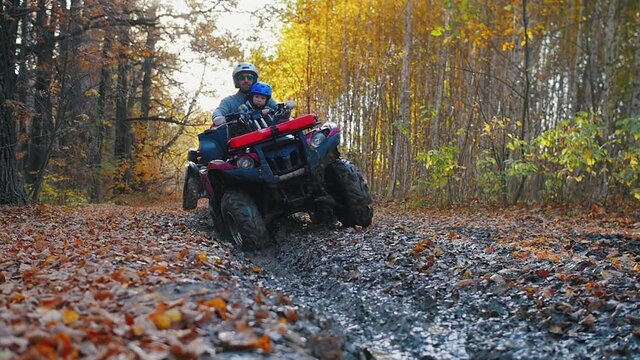 Outdoor activity - a man with his son and accompanying person riding ATVs in the forest - ride in the mud