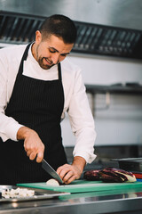 Portrait of a professional chef slicing eggplant over a green board in the restaurant kitchen