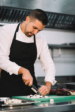Portrait of a professional chef slicing eggplant over a green board in the restaurant kitchen