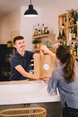 Portrait of a professional waiter handing to a customer a takeaway order in a recycled paper bag at the restaurant.