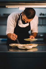 Portrait of a male chef with mask decorating food in ceramic dishes over stainless steel worktop in restaurant kitchen during coronavirus pandemic.