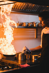 Portrait of a professional chef sautéing ingredients in a pan with large flare of oil