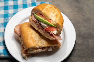 Mexican ham sandwich with avocado and cheese also called torta on dark background