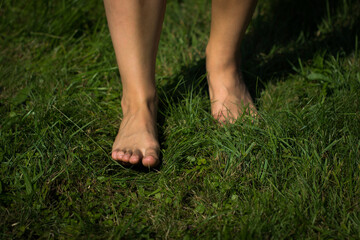 Woman's barefoot walking on the fresh, green grass in the sunny morning. Healthy lifestyle.
