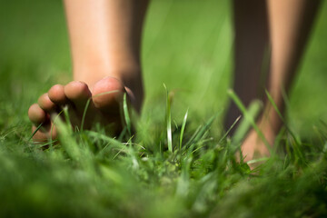 Woman's barefoot walking on the fresh, green grass in the sunny morning. Healthy lifestyle.