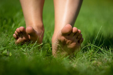 Woman's barefoot walking on the fresh, green grass in the sunny morning. Healthy lifestyle.