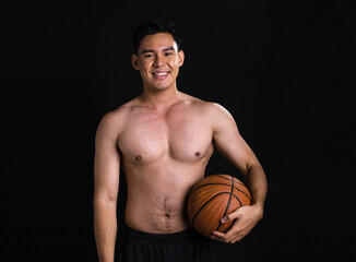 Obraz premium Portrait of asian muscular man standing and holding basketball on black background