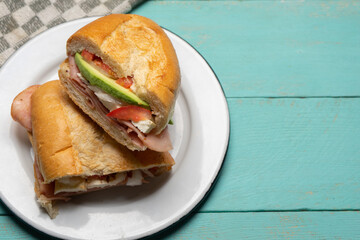 Mexican ham sandwich with avocado and cheese also called torta on turquoise background