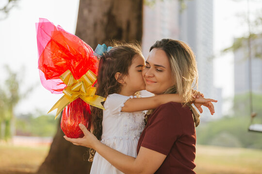 Latin family celebrating Easter. Curly girl kissing her mother on a sunny day in the park