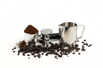 Black and silver coffee filter piled high with grounds sitting next to a tamper and milk steamer cup, beans surround the base