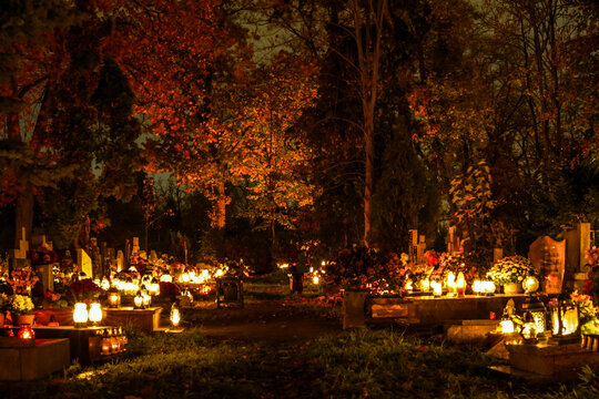 Many lit grave lights on All Souls' Day. Grave memorial candles in the cemetery. Cemetery alley at night. 