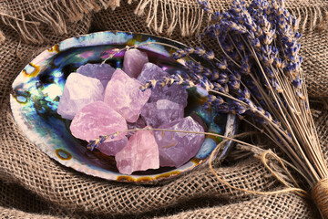 A top view image of rose quartz healing crystal in an abalone shell with dried lavender flowers. 