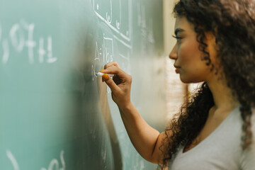 Latin student in the classroom. curly haired woman student writing assignments on blackboard during...