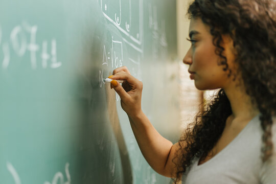 Latin student in the classroom. curly haired woman student writing assignments on blackboard during class