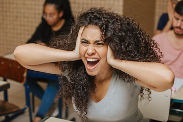 Latin students in the classroom. Curly haired student screaming sitting in the classroom with her hands on her head