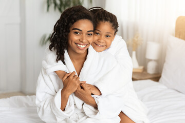 Home Portrait Of Happy Black Mommy And Daughter Wearing Bathrobes And Cuddling