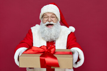 Happy funny old bearded Santa Claus wears costume holds present, Merry Christmas giftboxes wrapped with red ribbon, laughing giving gift box having fun isolated on red xmas background.