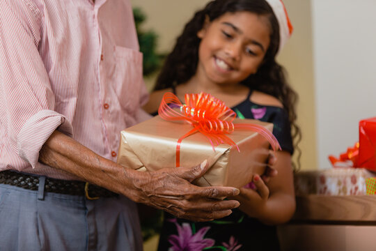 Summer Christmas dinner in Brazil. Real Brazilian family having fun at the Latin American Christmas party. old man giving a gift to curly haired child