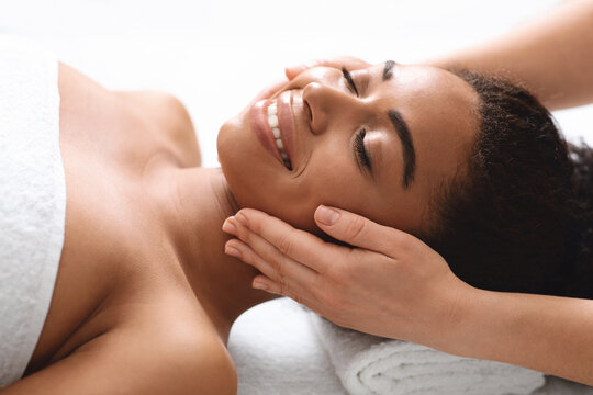 Smiling black woman having lifting face massage at spa