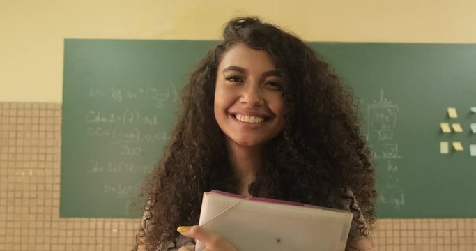 Latin student smiling wearing backpack holding a notebook in a classroom