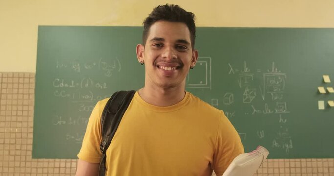 Latin student smiling wearing backpack holding a notebook in a classroom