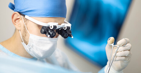 Male doctor surgeon in the operating room operates using binocular glasses microscopes.