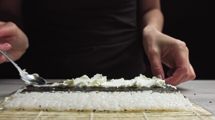 Close up of female hands of professional chef in gloves making delicious sushi rolls in restaurant kitchen
