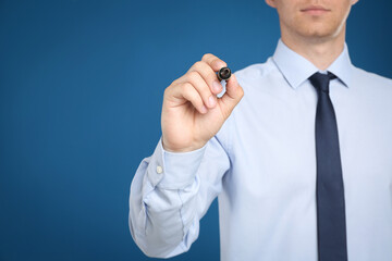 Businessman with marker against blue background, focus on hand. Space for text