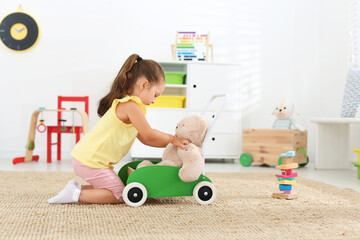 Cute little girl playing with toy walker and teddy bear on floor at home