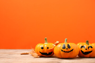 Pumpkins with scary faces and fallen leaves on orange background, space for text. Halloween decor