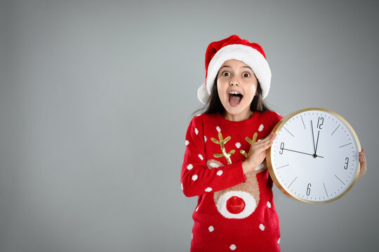 Girl in Santa hat with clock on grey background, space for text. New Year  countdown - Powered by Adobe