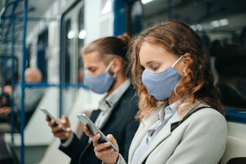 man and a woman with smartphones sitting in a subway car.