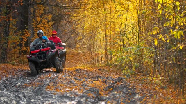 Three people riding atv in the autumn forest on the muddy track