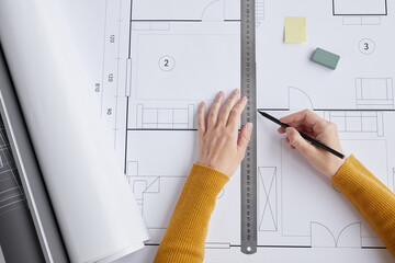 Top view close up of female architect drawing blueprints and plans while sitting at desk in office,...