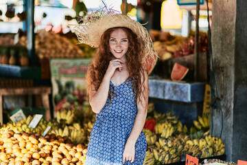 Young smiling redhead girl with freckles in blue dress and straw hat posing at the fruit market in Thailand. Copy space